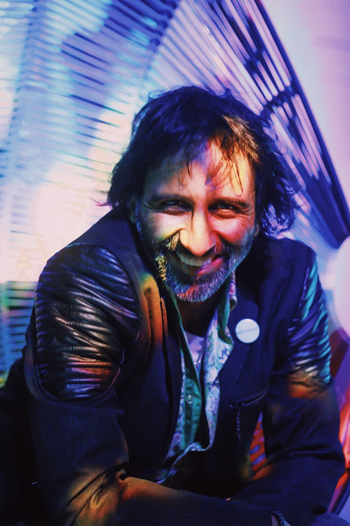 A man in a leather jacket smiling under blue and purple light
