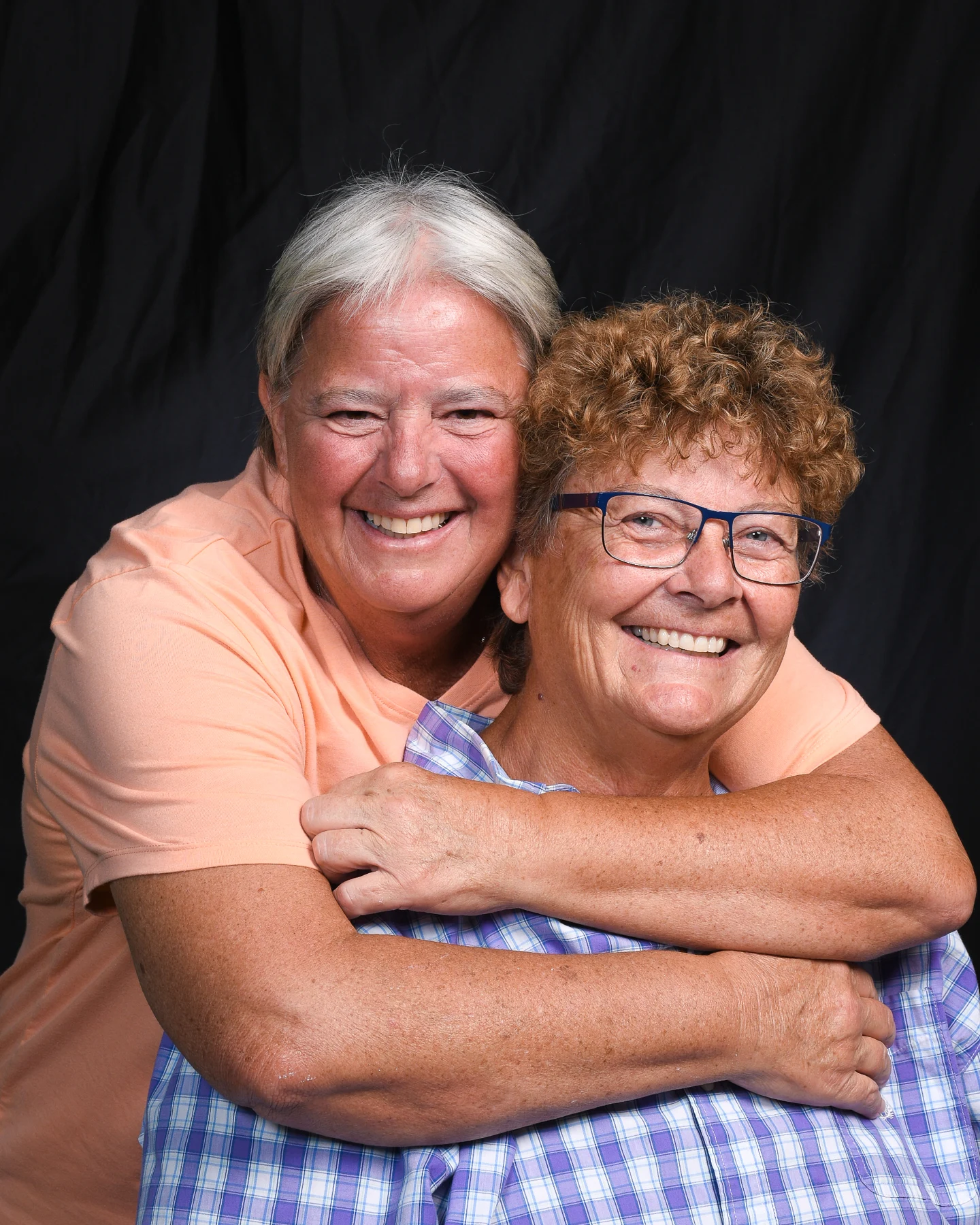 Two smiling women embracing against a dark portrait backdrop